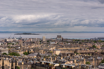 Obraz premium Edinburgh, Scotland, UK - June 13, 2012: Looking from Calton Hill over densely built Leith suburb towards the Nord Sea inlet under a heavy cloudscape. Island and other side of water.