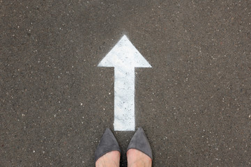 Fototapeta premium Woman standing near arrow on asphalt, top view. Choice concept