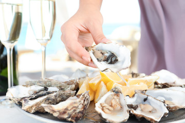 Woman holding fresh oyster over plate, focus on hand - Powered by Adobe