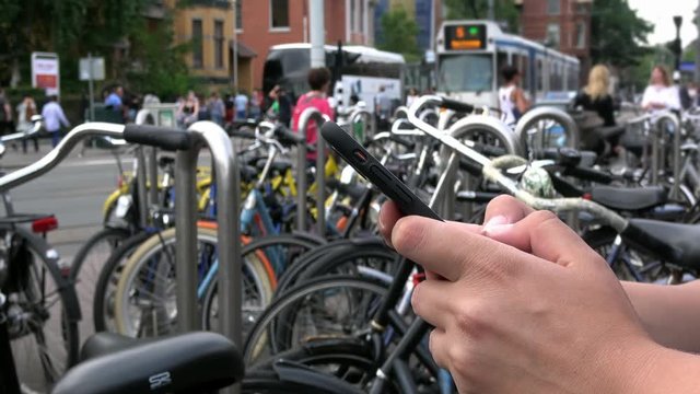 4K. Person using a smartphone. Close-up of hands typing on the phone, surfing the internet and checking social networks. Bicycles parked in Amsterdam, the tram is passing near-Adrian