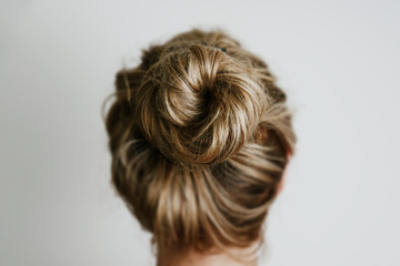 A view of the woman's hair from the back. Fashion and hairdressing concept. The girl, turned back, shows her hair bunched up in a bun on a light background.