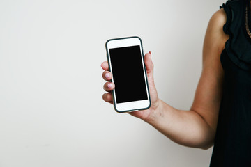Telephone in hand. The woman is holding a white telephone in hands with a blank display. Girl in a black blouse holds the phone in her hand, the concept of completing the content.