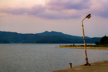 Inclining aged and rustic street light post near the lake in the evening.