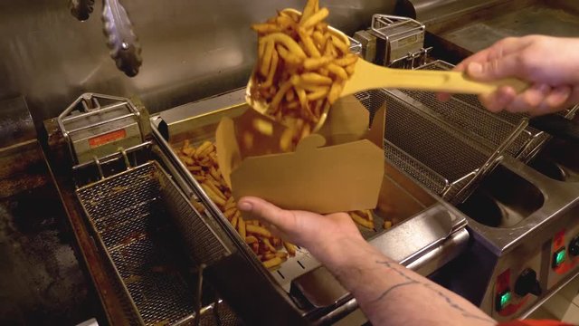 A cook fulfilling a box of delicious french fries.