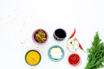 Different dip sauce in bowls near chili pepper and greenery. Ketchup, mayonnaise, mustard, soy sauce, barbecue sauce, pesto, mustard, sour on white background top view space for text