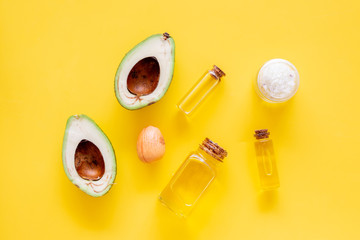 Cosmetics for skin care. Avocado oil near half of avocado on yellow background top view copy space