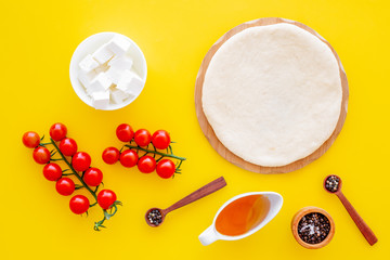 Ingredients for cooking vegetarian pizza. Rolled pizza dough, cherry tomatoes, olive oil, cheese mozzarella, spices on yellow background top view mockup
