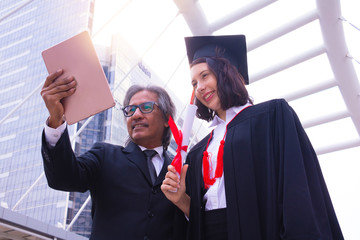 She is  Graduate and wearing  graduate's dress. They  are use smartphone. They are happy in good time. Photo concept  Education and success.