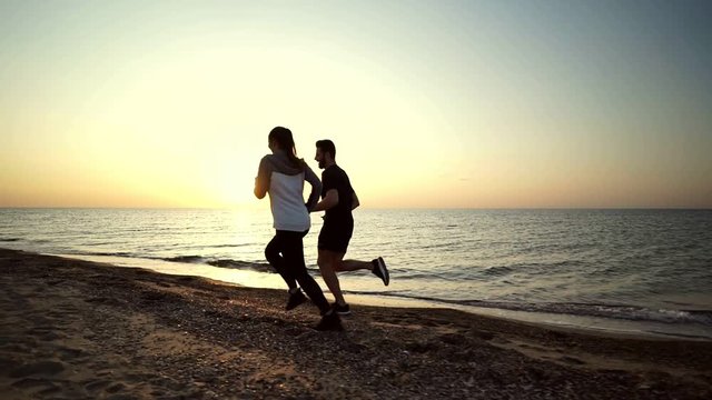 Side view of Young sports couple running toogether on beach near the sea