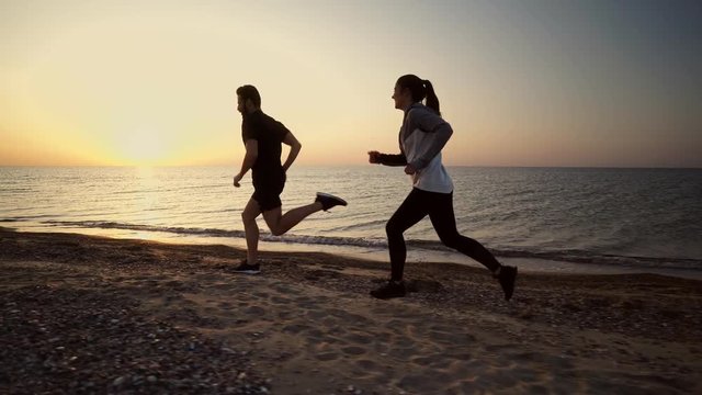 Side view of Happy sports couple running and having fun together on beach near the sea