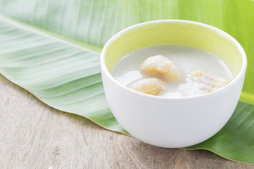 Banana in coconut milk in a white bowl on a banana leaf.