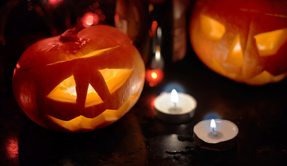 Two orange glowing carved pumpkin heads for the holiday of Halloween, stand on a table with candles on a dark background with burning red lanterns.