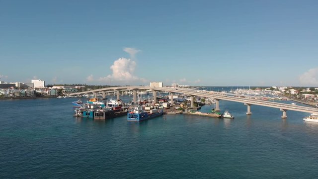 4K Cinematic Aerial flyover of boats and barges toward paradise island bridge as traffic passes by