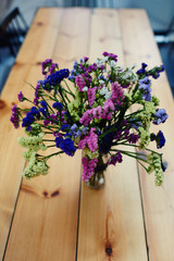 Long narrow table with a glass container with pink and green flowers on long stems. Colorful field flowers on a wooden table.