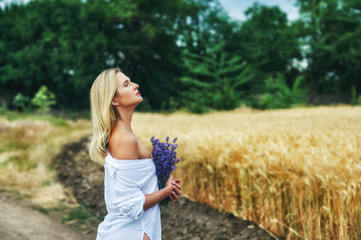 portrait of a young romantic woman on a walk in the countryside . Woman with a bouquet of lavender at a wheat field