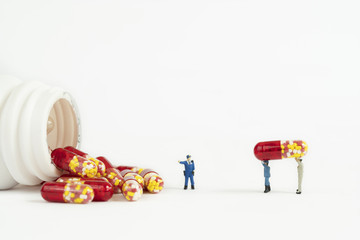 Antibiotic drug capsule with miniature peope on white background
