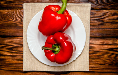 Two red peppers lying on a brown background 