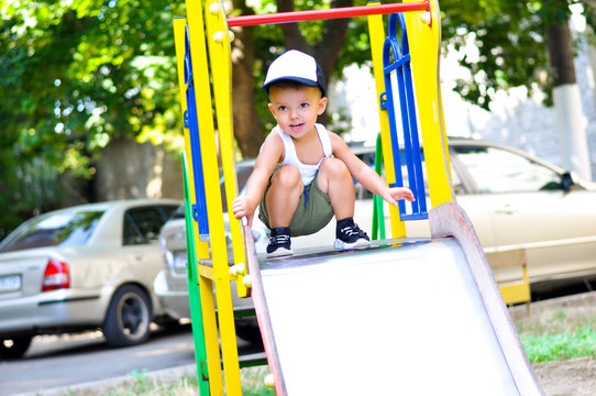 A cute two-year-old boy in a baseball cap sliding down on a slide on a playground
