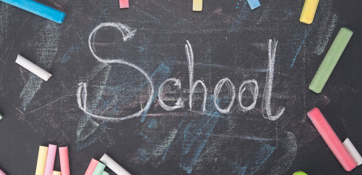 a set of colored crayons, scattered on a black board, in the center of the inscription-school