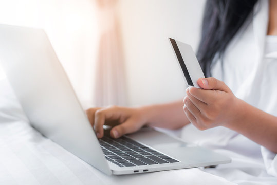 Pretty attractive Asian woman shopping online by laptop with credit card, laying on the bed at bedroom 