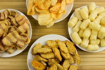 Snack corn and potato chips on a plate. Wooden table. Salty food for beer