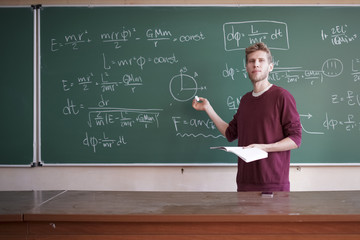 young professor teacher with microphone standing near the blackboard and speaking on the university...