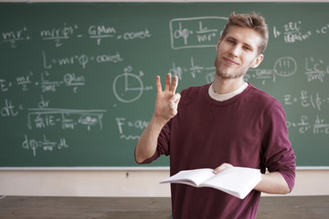 online physics course young male teacher thumb up in classroom with chalkboard with formulas copy...