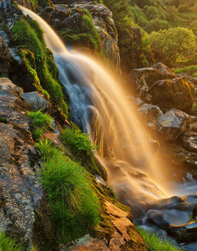 Long exposure waterfall glowing with sunset light, from the Loup of Fintry in Scotland (UK).