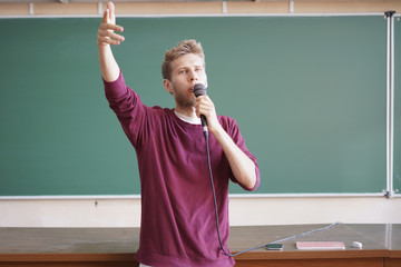 young professor teacher speaking with the microphone in the lecture hall standing near the...
