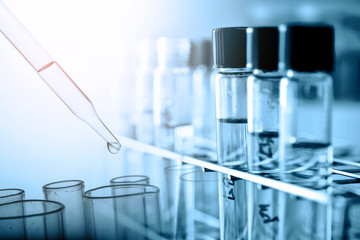 Dropping chemical liquid to test tube with lab glassware background, science or medical research and development concept.