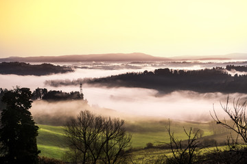 countryside cultivated with fog rising in the morning sunlight