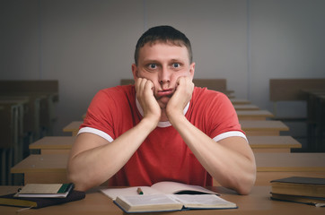 Tired from study a student boy is sitting by the school desk.