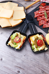 Delicious traditional Swiss melted raclette cheese on diced boiled or baked potato served in individual skillets with salami..