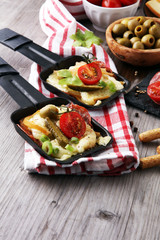 Delicious traditional Swiss melted raclette cheese on diced boiled or baked potato served in individual skillets with salami..