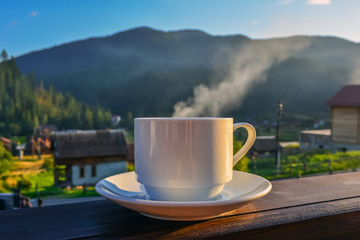 a cup of tea, coffee, standing on the porch of the hotel balcony, overlooking the mountains, in the early morning in the sunlight