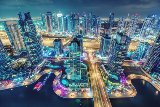 Scenic nighttime skyline of big modern city with illuminated skyscrapers. Aerial view of Dubai Marini, UAE. Multicolored travel background.