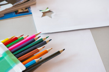 Creative workshop for kids. Pile of sharp coloured drawing pencils on table. Cutting out stars and making decorations from white paper. Concept of art, crafts and kids having fun