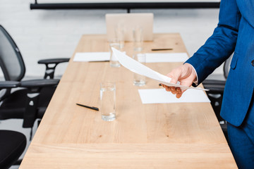 cropped shot of businessman holding blank paper over conference table at office