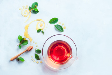 Glass cup of tea with decorative honey swirls and green leaves. Home remedies flat lay on a white background with copy space
