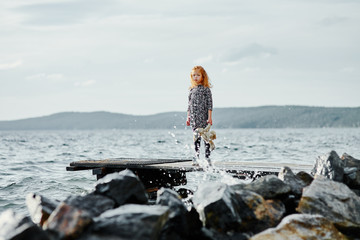 A sad child with a toy stands on the pier by the sea and looks a