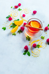 Honey tea from above. Decorative honey swirls, lemon slices, berries and tea in a glass cup on a white wooden background with copy space. Creative food flat lay