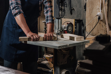partial view of woodworker using electric drill on wood at workshop