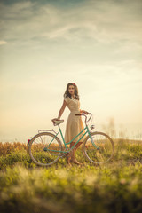 pretty young smilling woman with retro bicycle in sunset on the road, vintage old times, girl in retro style on meadow