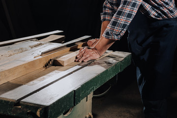 partial view of carpenter using saw at wooden workshop