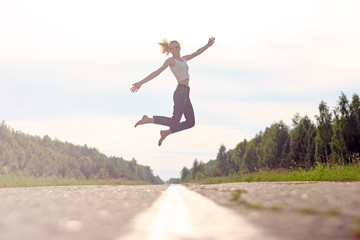Happy young woman jumping having fun outdoors on the road. concept of freedom.girl flies