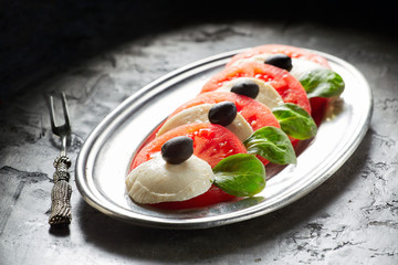 Caprese salad on a metal platter with fork and on a dark background
