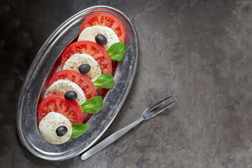 Caprese salad on a metal platter with fork and on a dark background