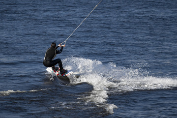 A man on a blue sea on a white spray wakeboard.