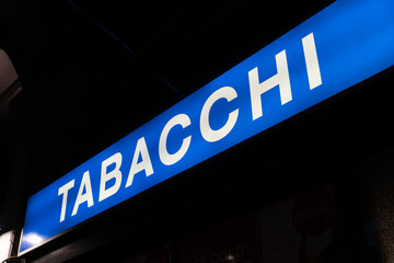 Obraz premium Blue signage of a Tabacchi, Italian for Tobacco shop, on a black background. Also called a tobacco shop, a tobacconist's shop or a smoke shop, it is a retailer of tobacco products