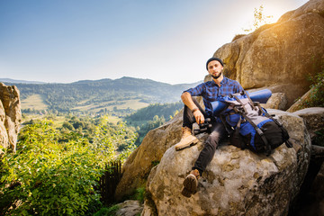 Tired man traveler sitting on the rocks and holding a backpack